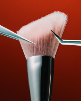 Close-up of a makeup brush's bristles held with tweezers against a deep red background, editorial beauty product photography 