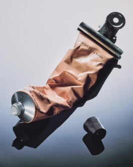 Angled beauty product tube styled with a bulldog clip against a soft grey gradient background, commercial still life photography by Camilo Bustamante 